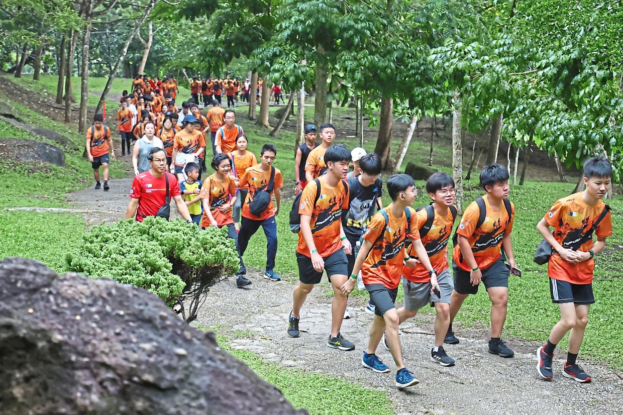 Hikers walking with family and friends amid the lush greenery and cool morning air. (Right) Participants gathering at the field in Penang City Park.