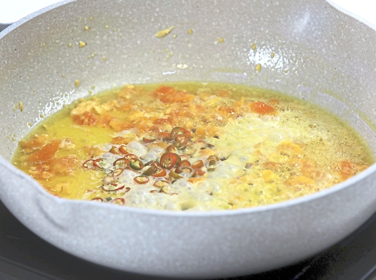 Melt the butter in the wok, then stir in mashed yolks with chillies, evaporated milk, sugar and bouillon until the mixture becomes a thick and foamy paste.