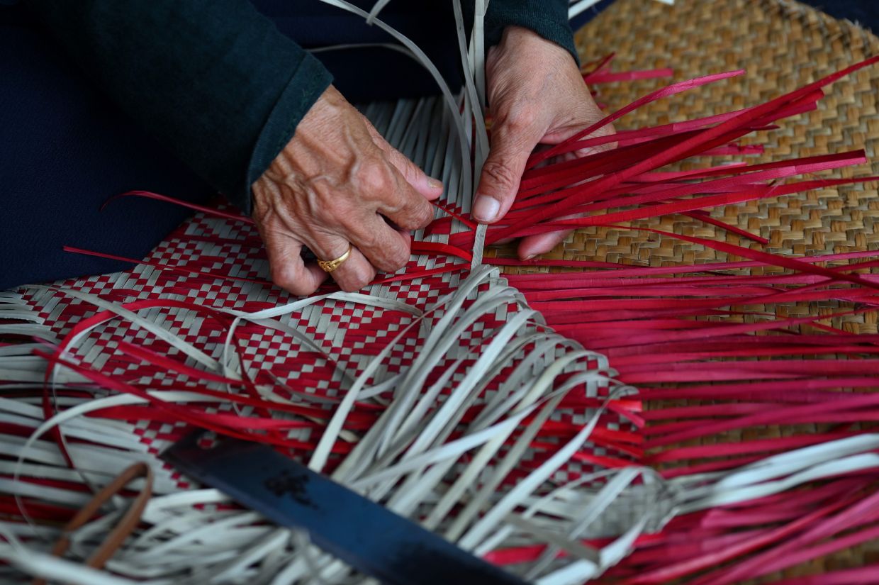 A close-up of Asmah weaving mengkuang strips into a mat. - Photo: Bernama