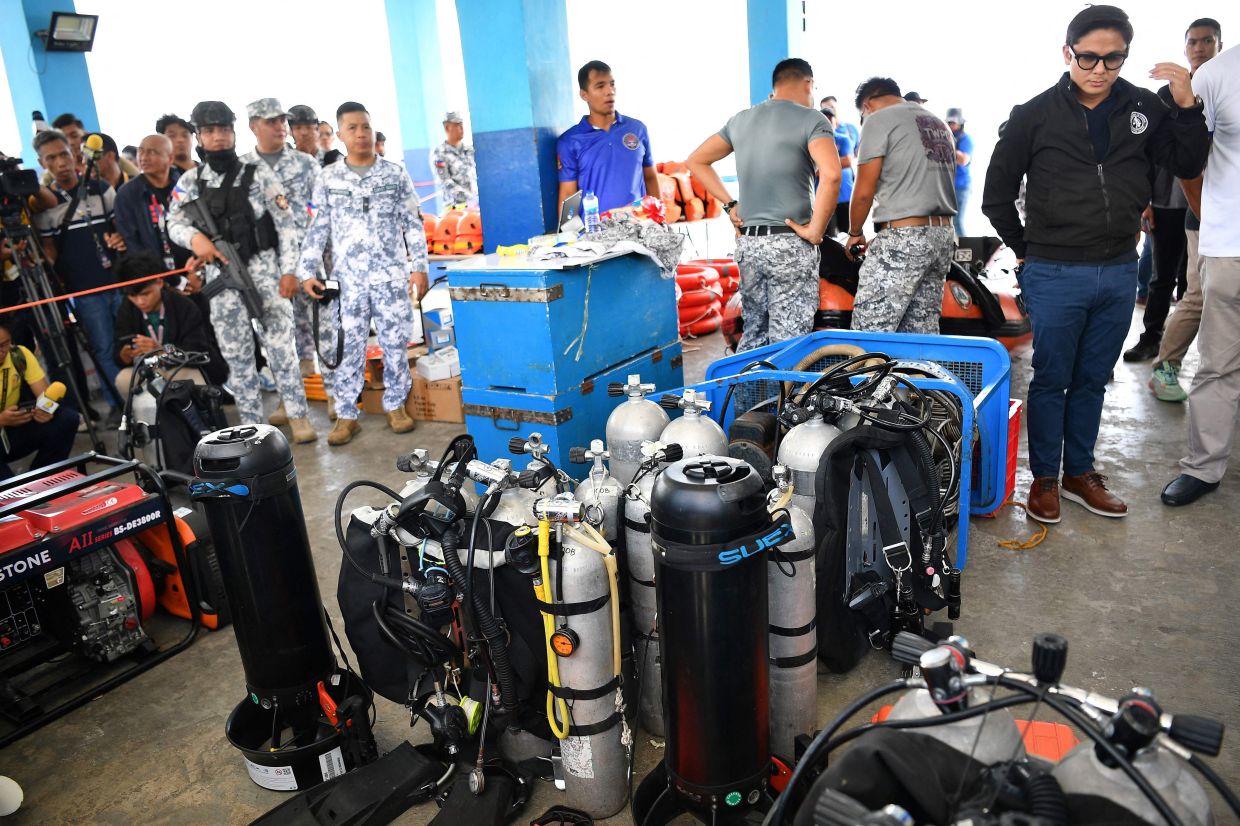 Philippine officials led by Assistant Secretary Mico Clavano (R) of the Departnment of Justice inspect diving gear of the Philippine coast guard prior to their search and retrieval operation for the bodies of cockfighters who were allegedly dumped in Taal Lake, in Talisay town, Batangas province South of Manila. Search teams began scouring a lake south of the Philippine capital Manila for dozens of cockfighters allegedly murdered by rogue police. -- Photo by Ted ALJIBE / AFP