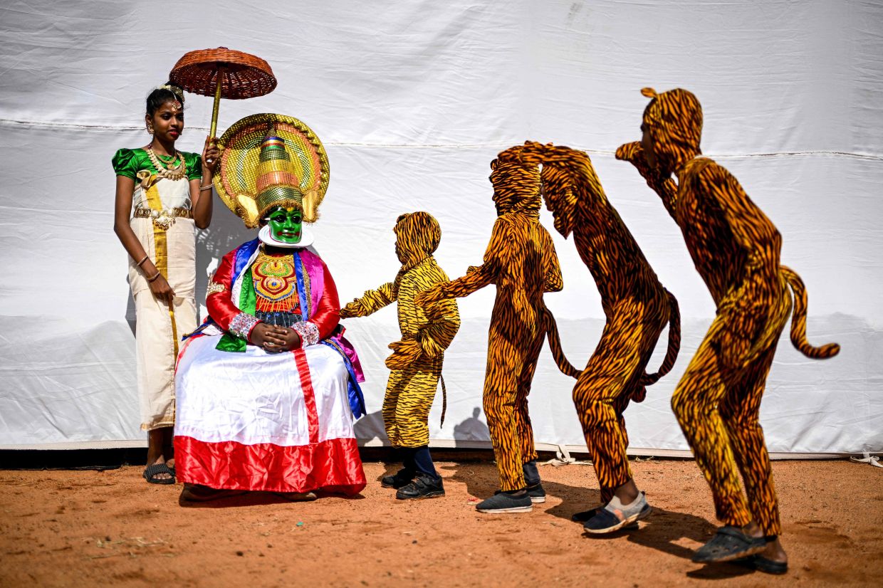 A Kathakali classical dancer (sitting) watches artists rehearse the traditional folk dance Pulikkali (Tiger Dance) as they wait backstage before their performance at a cultural festival in Chennai on July 12, 2025. -- Photo by R. Satish BABU / AFP