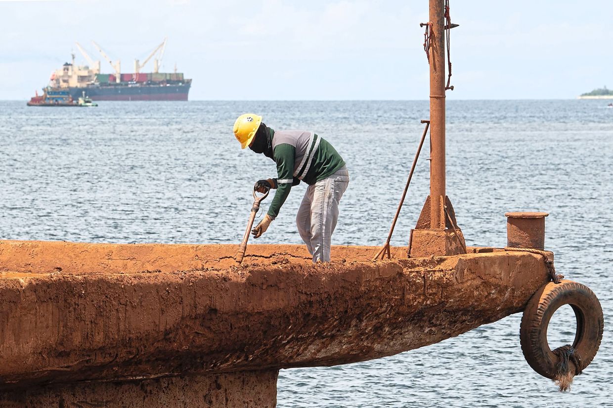 A worker shovelling leftover nickel ore minerals at a pier in the village of Rio Tuba. — AFP