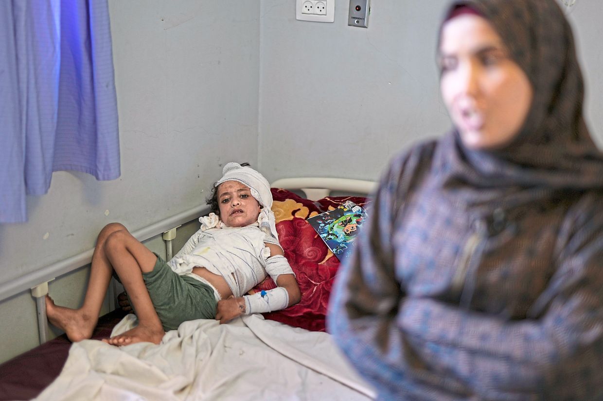 Iman standing near Hamza, who lies in bed with third-degree burns caused when he was frightened by an Israeli airstrike, at Nasser hospital in Khan Yunis, Gaza. — AP