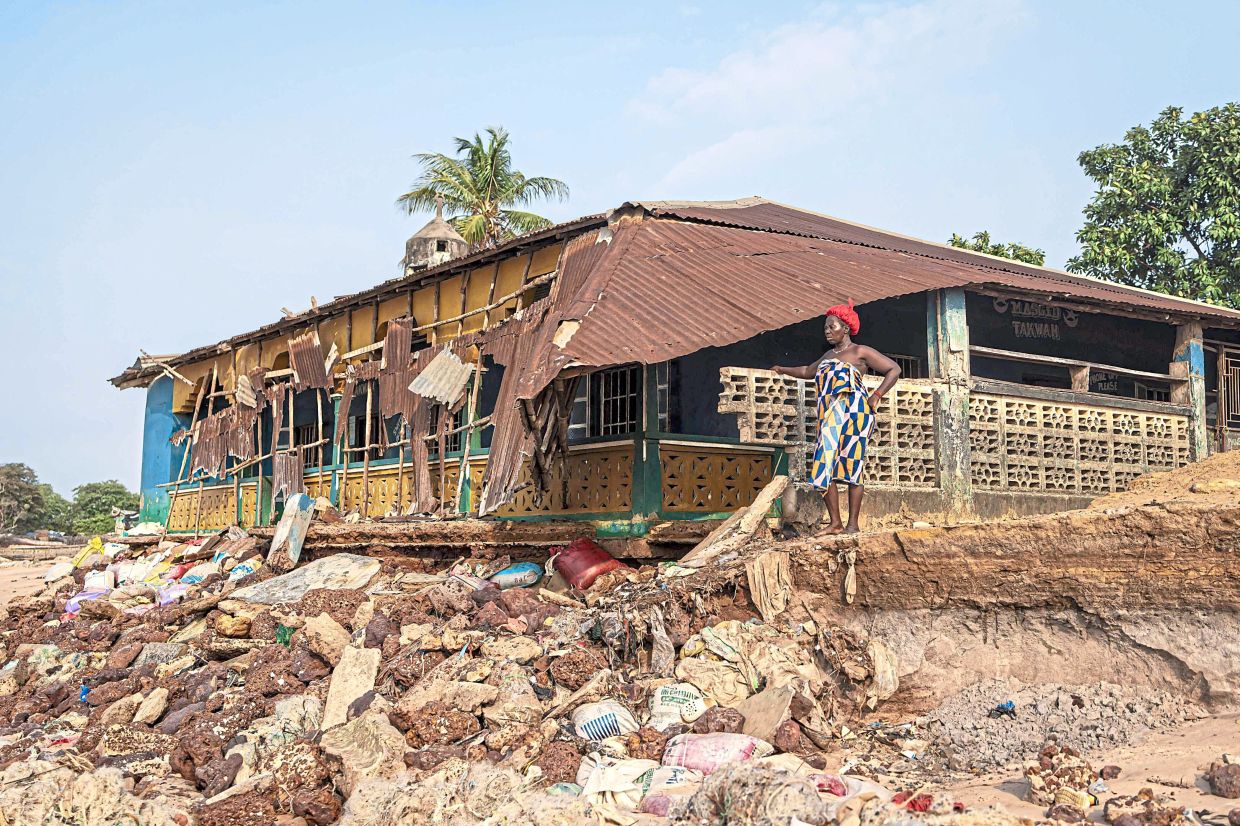 A resident stands next to a section of a Mosque that collapsed due to the effects of rising sea levels in Plantain Island.