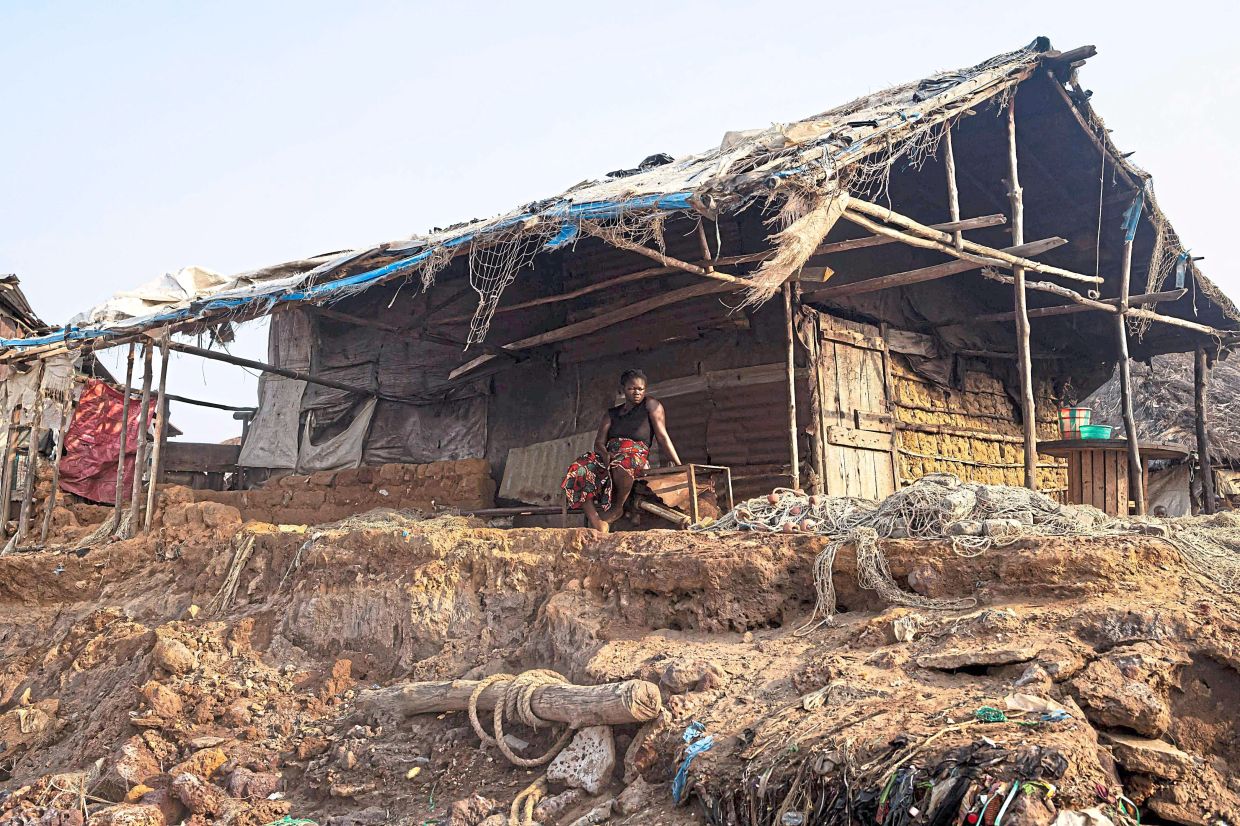 A resident sits outside Ousmane 'Shorty' Kamara's house that was damaged by the effects of rising sea levels in Plantain Island.