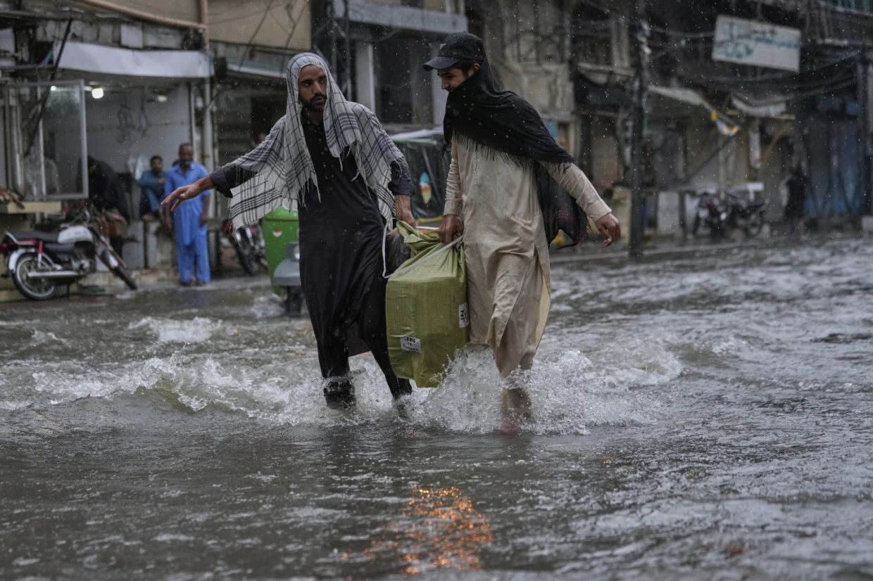 Local residents carry a big bag as they walk through a flooded road during monsoon rainfall, in Rawalpindi, Pakistan, Thursday (July 17, 2025). - Photo: AP