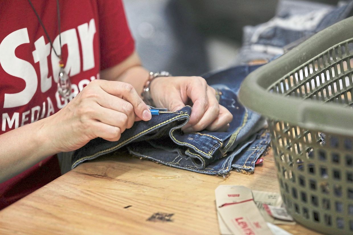 A volunteer using a seam ripper to unpick stitches of an old pair of jeans.