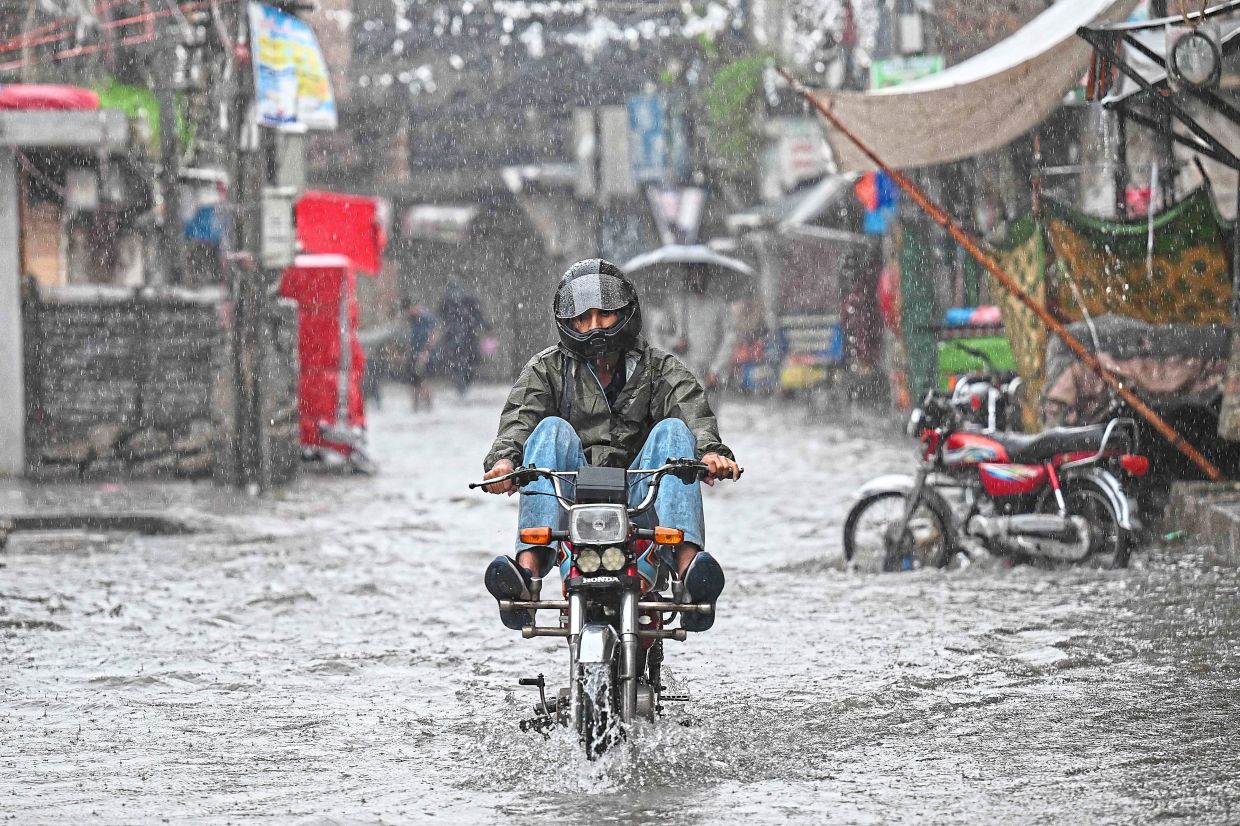 Coming through: A man on a motorbike wading through a flooded street during heavy monsoon rains in Rawalpindi. — AFP