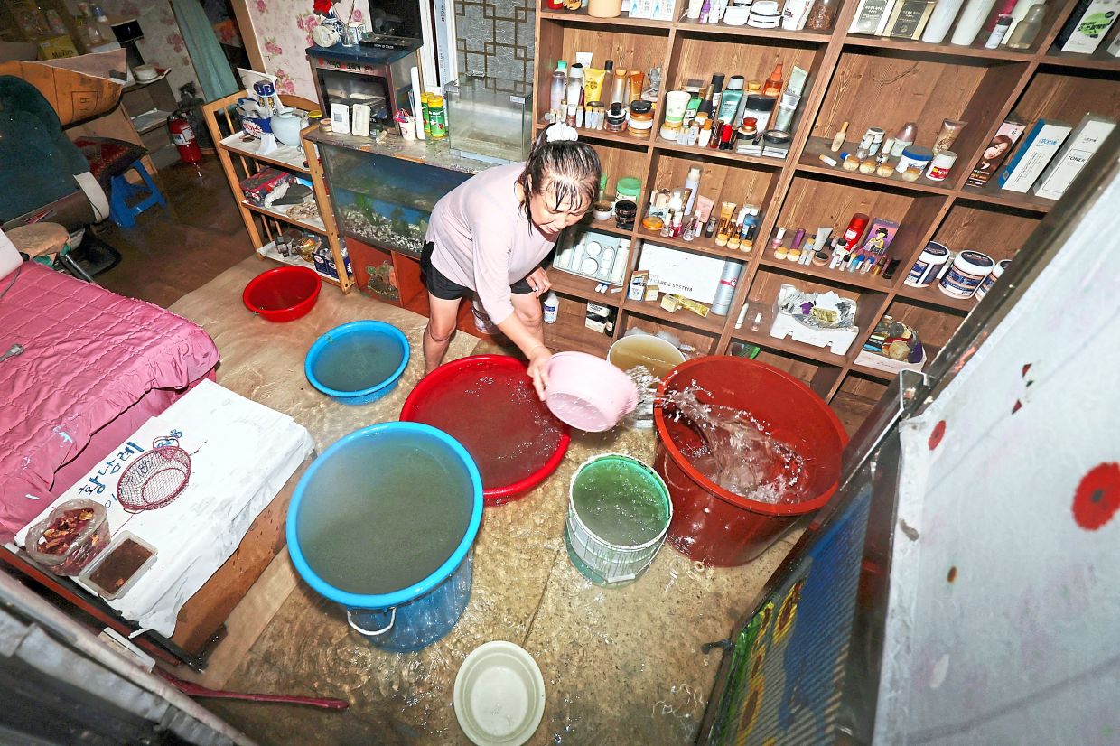 The aftermath: A woman cleaning the flooded floor of her hair salon caused by torrential rain in Gwangju; (below) and Fire Services rescue members searching for missing people after a 10m-high (33-foot) retaining wall from an overpass collapsed onto the road in Osan. — Reuters/AFP 