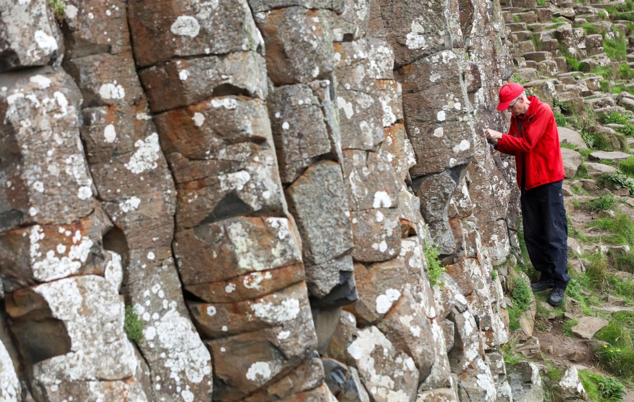 National Trust's Nature Engagement Officer, Cliff Henry, looks for coins left by tourists in the cracks of the stones at the Giant's Causeway. — AFP 
