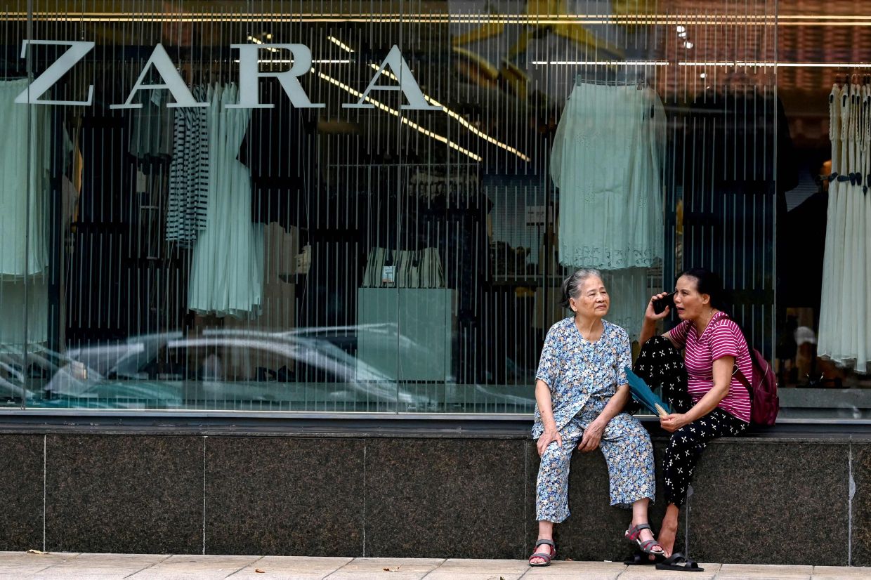 Women relaxing in front of a fashion store in Hanoi. -- Photo by Nhac NGUYEN / AFP