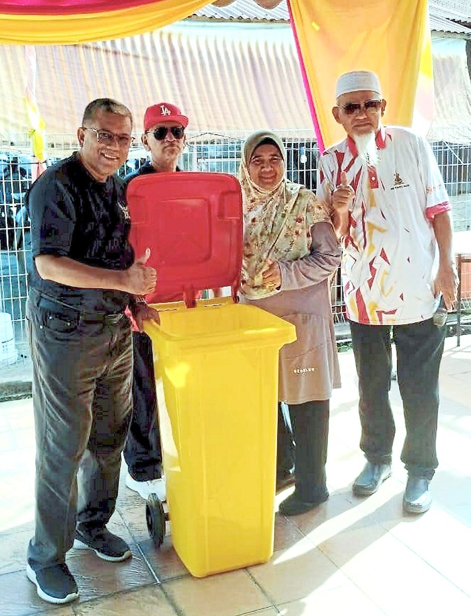 Mazwan (left) showing a sample of the bin that will be distributed to Kampung Sungai Ramal Dalam residents who have subscribed to the waste collection services. Looking on are Kamsari (right) and other villagers.