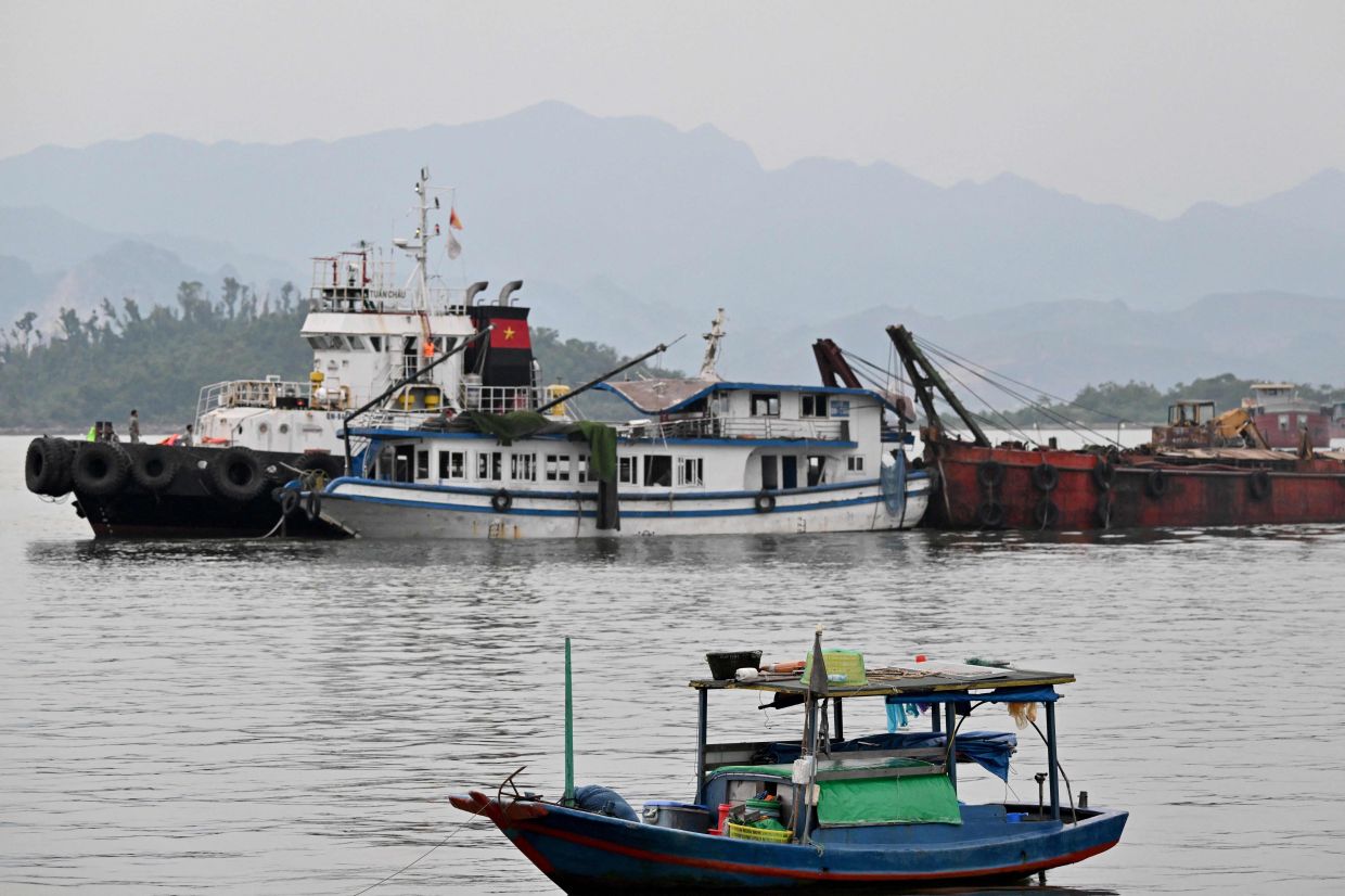 The tourist boat (centre) that capsized is towed back to the port in Ha Long bay, Quang Ninh province on July 20, 2025. A tourist boat ferrying families around Vietnam's Ha Long Bay capsized in a storm on on July 19 afternoon, leaving at least 34 people dead, according to state media reports, as rescuers scrambled to locate the missing. - Photo: AFP
