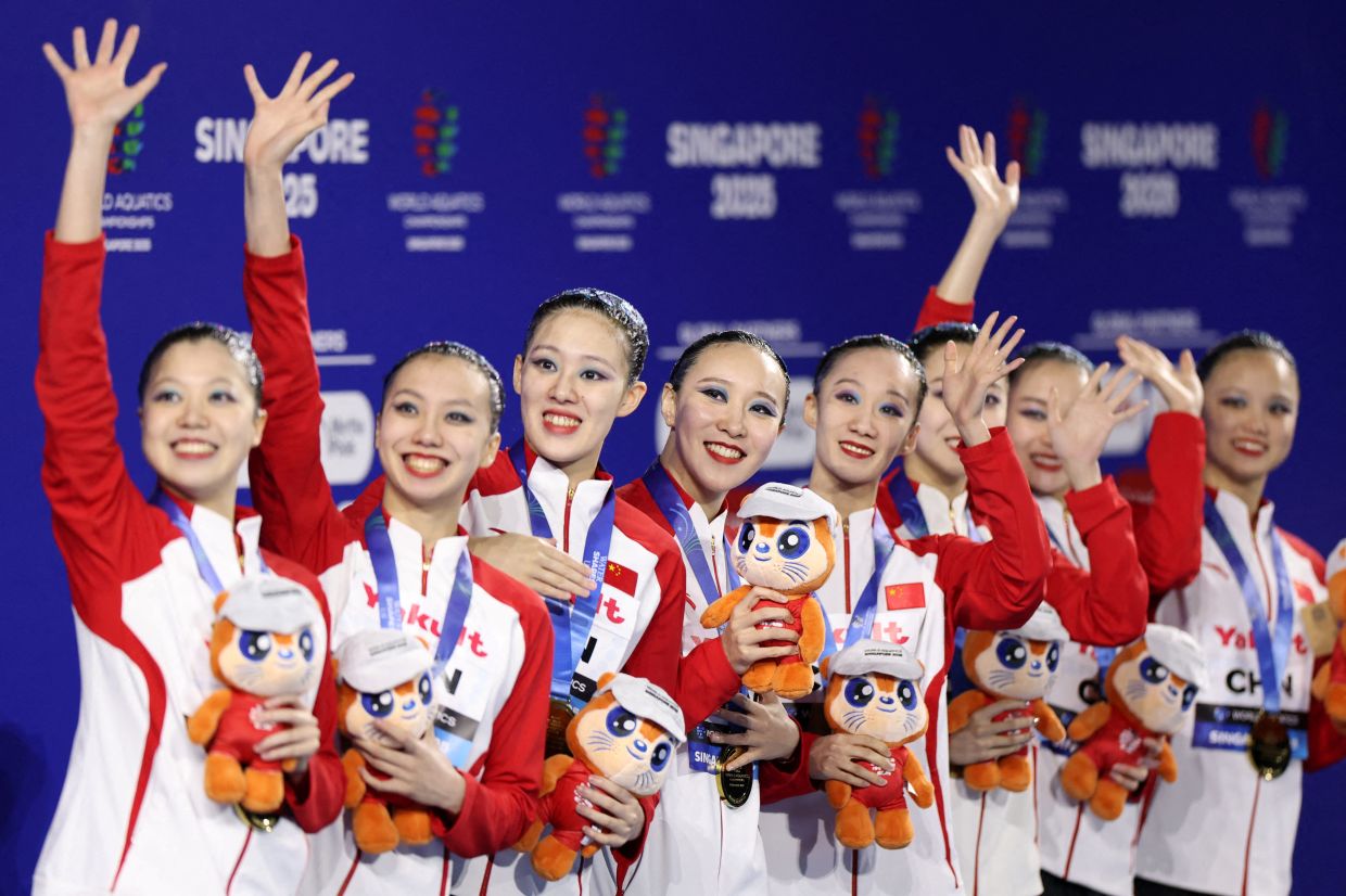 Artistic Swimming - World Aquatics Championships - Team Free Final - World Aquatics Championships Arena, Singapore - Sunday, July 20, 2025; Gold medalists Team China celebrate on the podium with medals and mascots Ollie the Otter. -- Photo: REUTERS/Hollie Adams