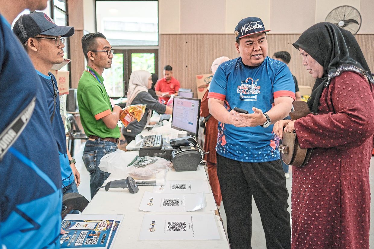 Left: KPDN officer Mohd Zulkiffli Sulaiman (second from right) explaining the eCOSS app to a customer during the Madani Rahmah Sales at Dewan Muafakat Kampung Bakar Batu. — Photos: Bernama