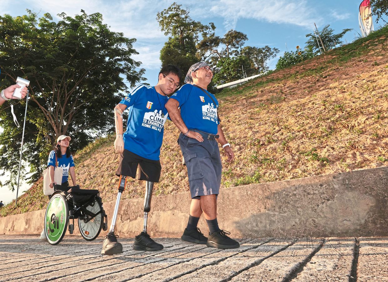 Courage in motion: (Top) Participants taking on the uphill challenge of climbing Iconic Hill during ‘Climb to Change a Life’ hiking event in Paya Terubong, Penang. (Inset) Zy Kher and his father making their way up the hill. — ZHAFARAN NASIB/The Star