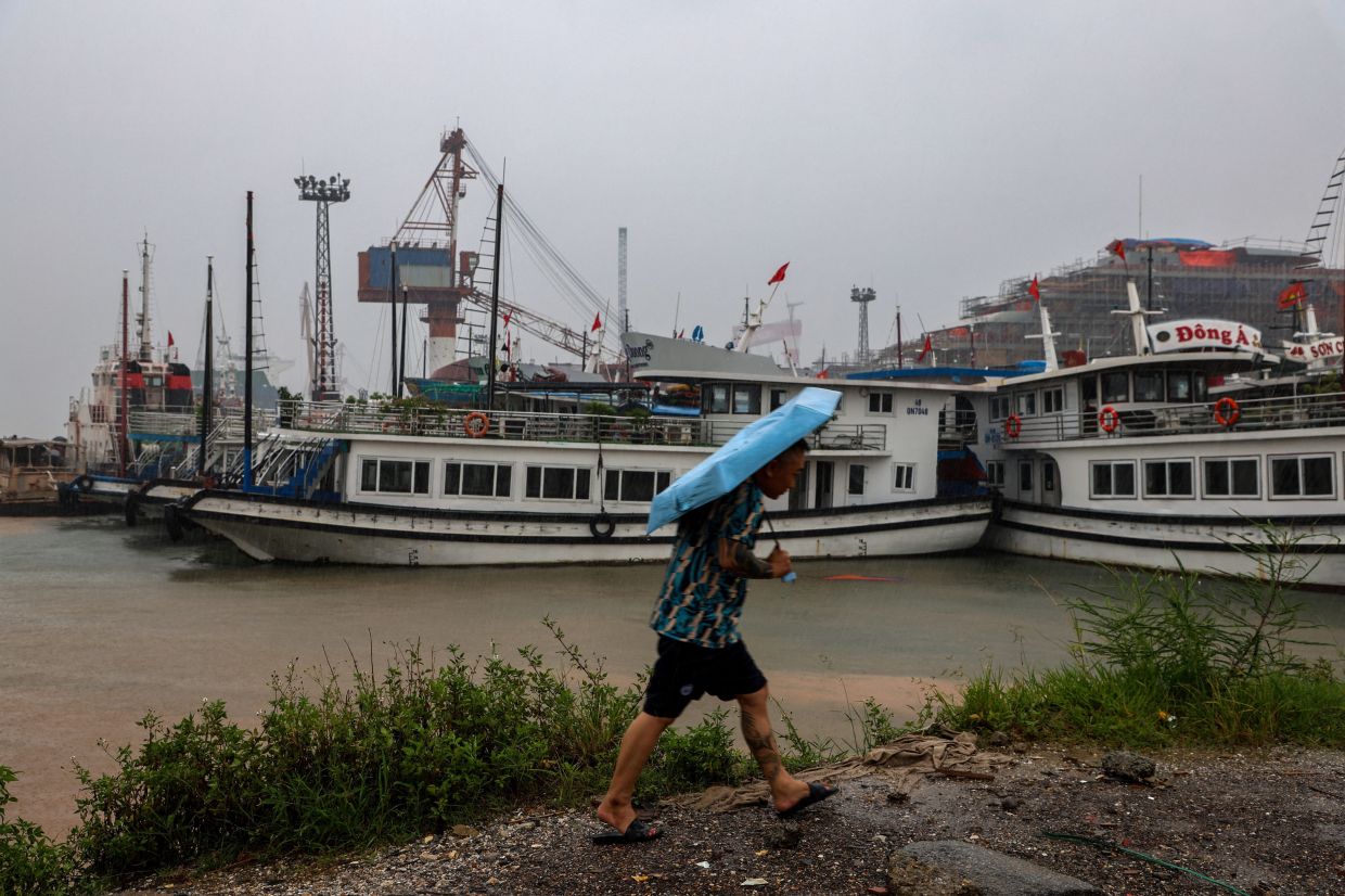 A man holding an umbrella walks near docked tourist boats, as Typhoon Wipha approaches, at Halong Bay, Quang Ninh province, Vietnam, on Monday, July 21, 2025. -- Photo: REUTERS/Thinh Nguyen