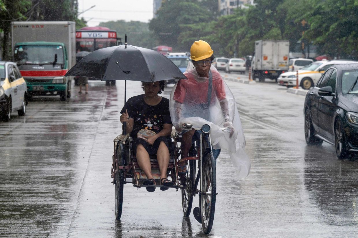 A trishaw driver rides as his passenger uses an umbrella to cover themselves from the rain in Yangon on Monday, July 21, 2025. -- Photo by Sai Aung MAIN / AFP