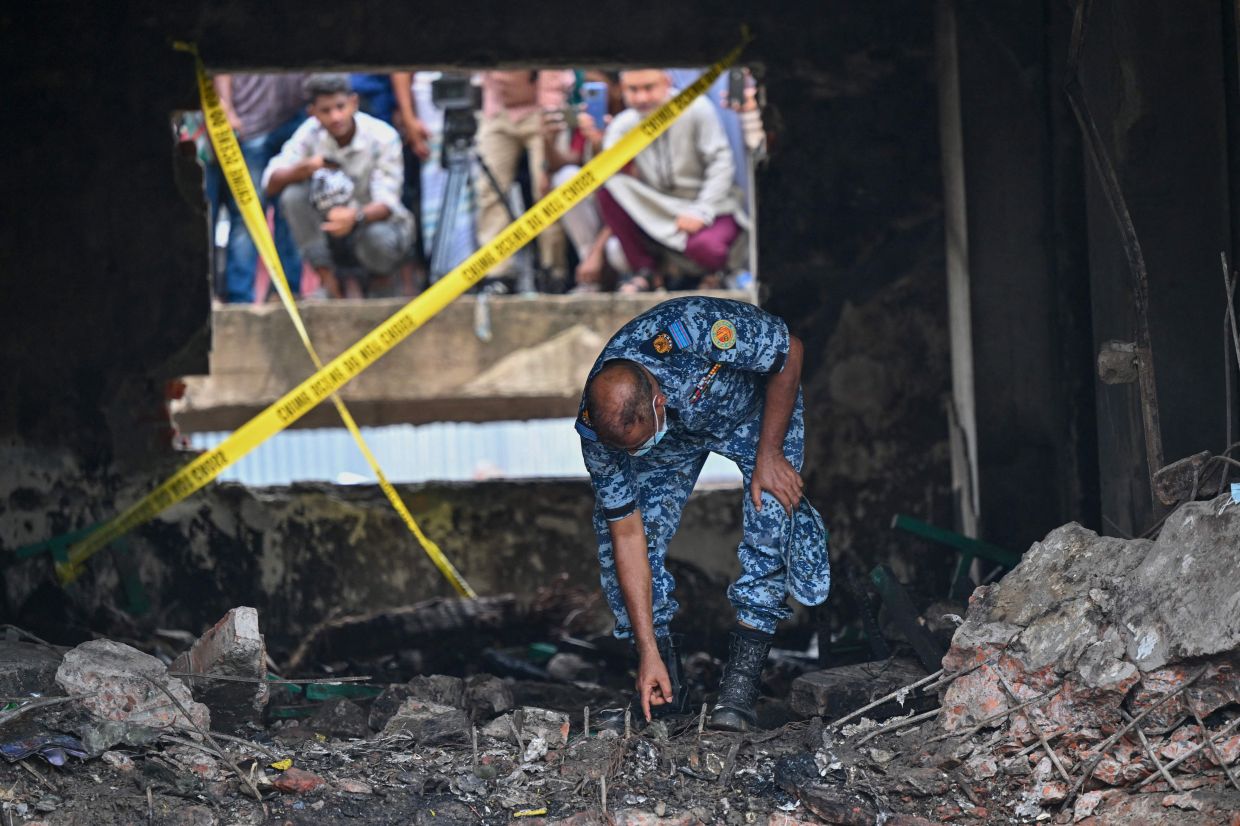 A Bangladesh Air Force personnel inspects the crash site a day after a training jet crashed into a school in Dhaka on July 22, 2025. A Bangladeshi fighter jet crashed into a school in the capital Dhaka on July 21, 2025. - Photo: AFP
