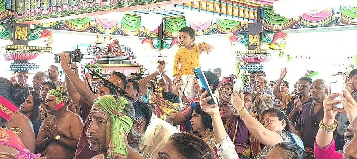A boy being lifted up by his parents to witness the divine blessings of Goddess Mariamman at the temple.
