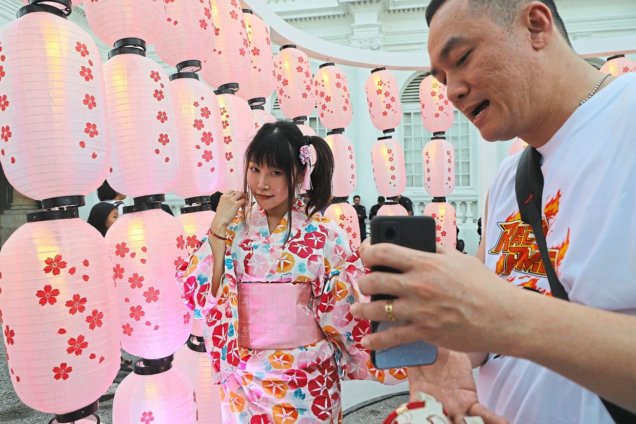 Visitor Vincent Chuah, 40 (right), taking photos of friend Ice Goh, 30 (left), against the backdrop of lanterns at Penang Bon Odori 2025.