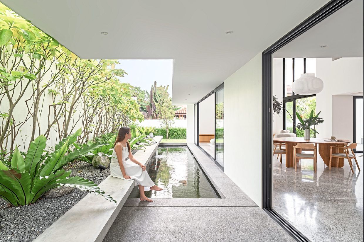 An elevated rock garden with lush greenery conceals a waterfall that trickles into a seating area at the outdoor deck.