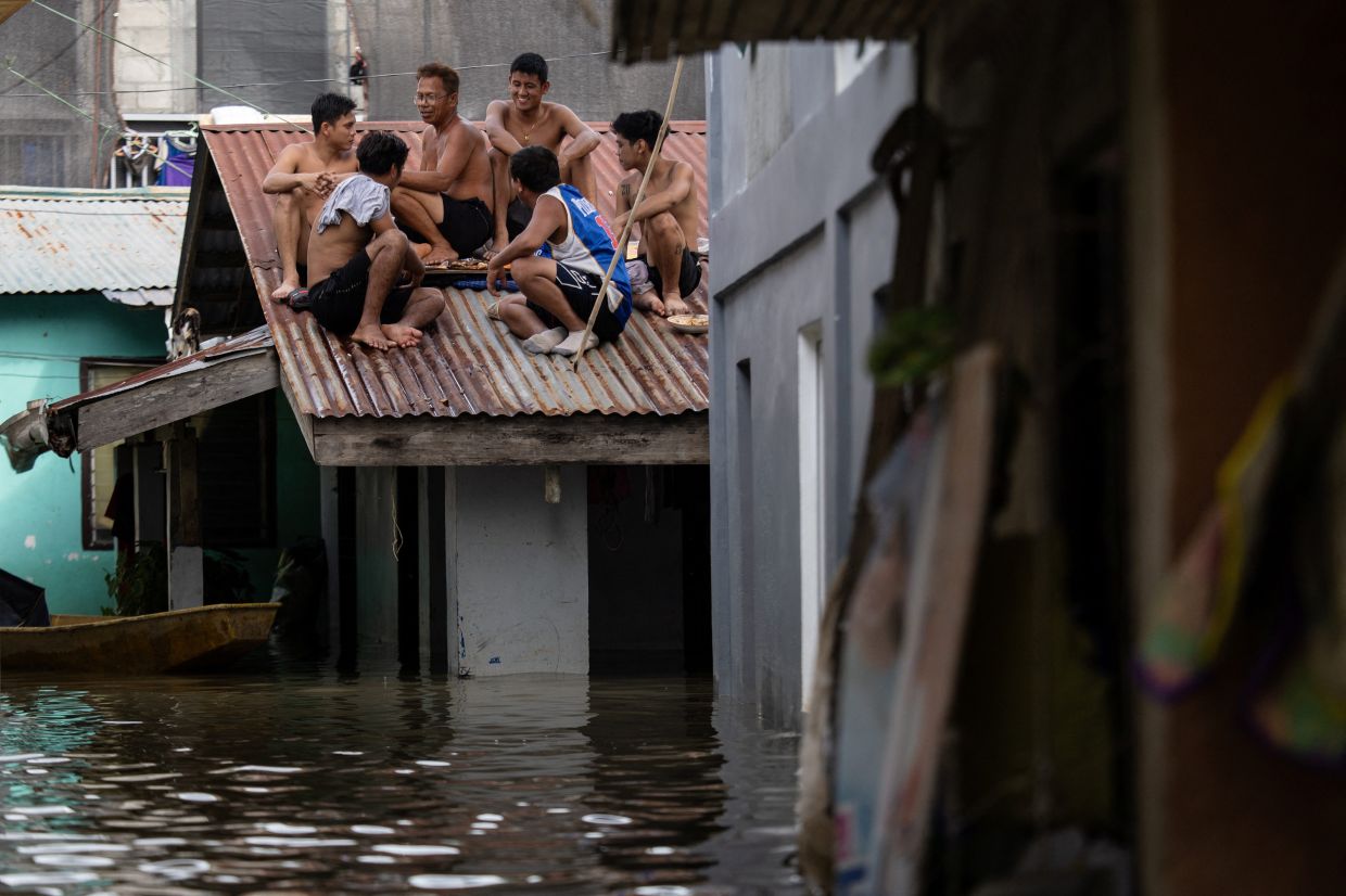 Flood victims sitting on the roof of a submerged home at a village inundated by high tide, and flooding brought by monsoon rains and Typhoon Co-may, in Calumpit, Bulacan, Philippines, on July 25, 2025. - Reuters