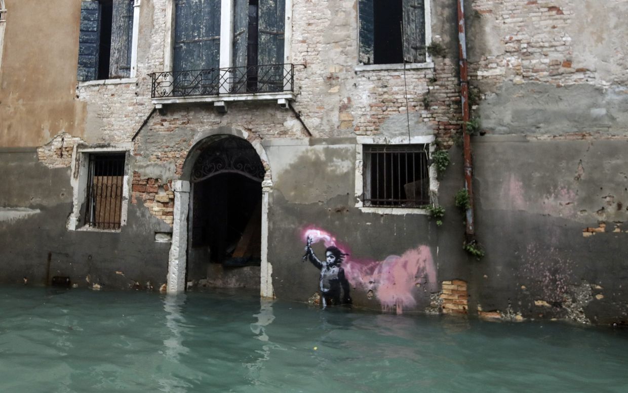 The Bansky work 'The Migrant Child' depicts a shipwrecked child holding a pink smoke bomb and wearing a lifejacket appeared along Rio di San Pantalon in Venice in May 2019. Photo: AP