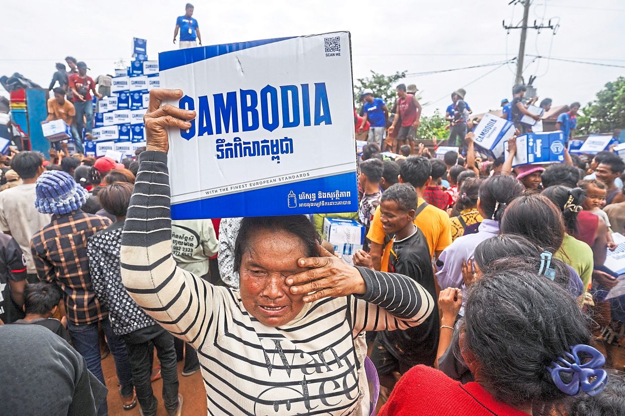 A woman holding a box of water donated at Batthkao Primary School camp. -Reuters