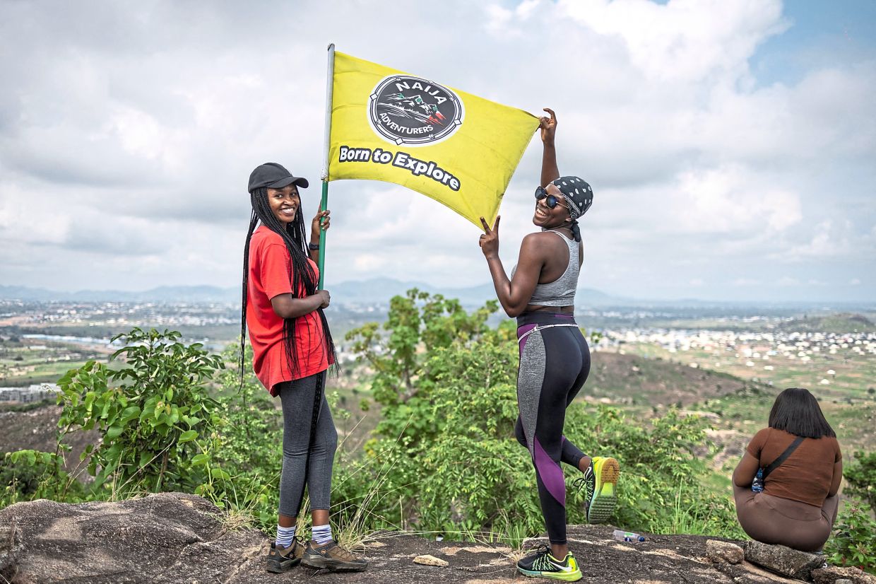 Hikers pose for a photograph with a Naija Adventurers flag at the summit of a hill.