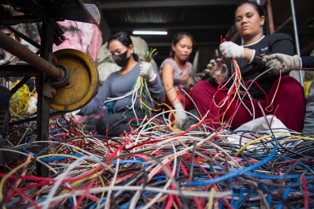 Workers removing copper from industrial wiring inside a recycling shop in Manila. - AFP