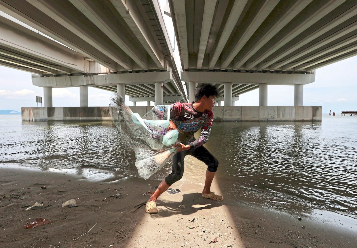 Nur Mohamad Abdul Jalil, 19, seen underneath Penang Bridge trying to get some shade while catching shrimps for fishing bait.