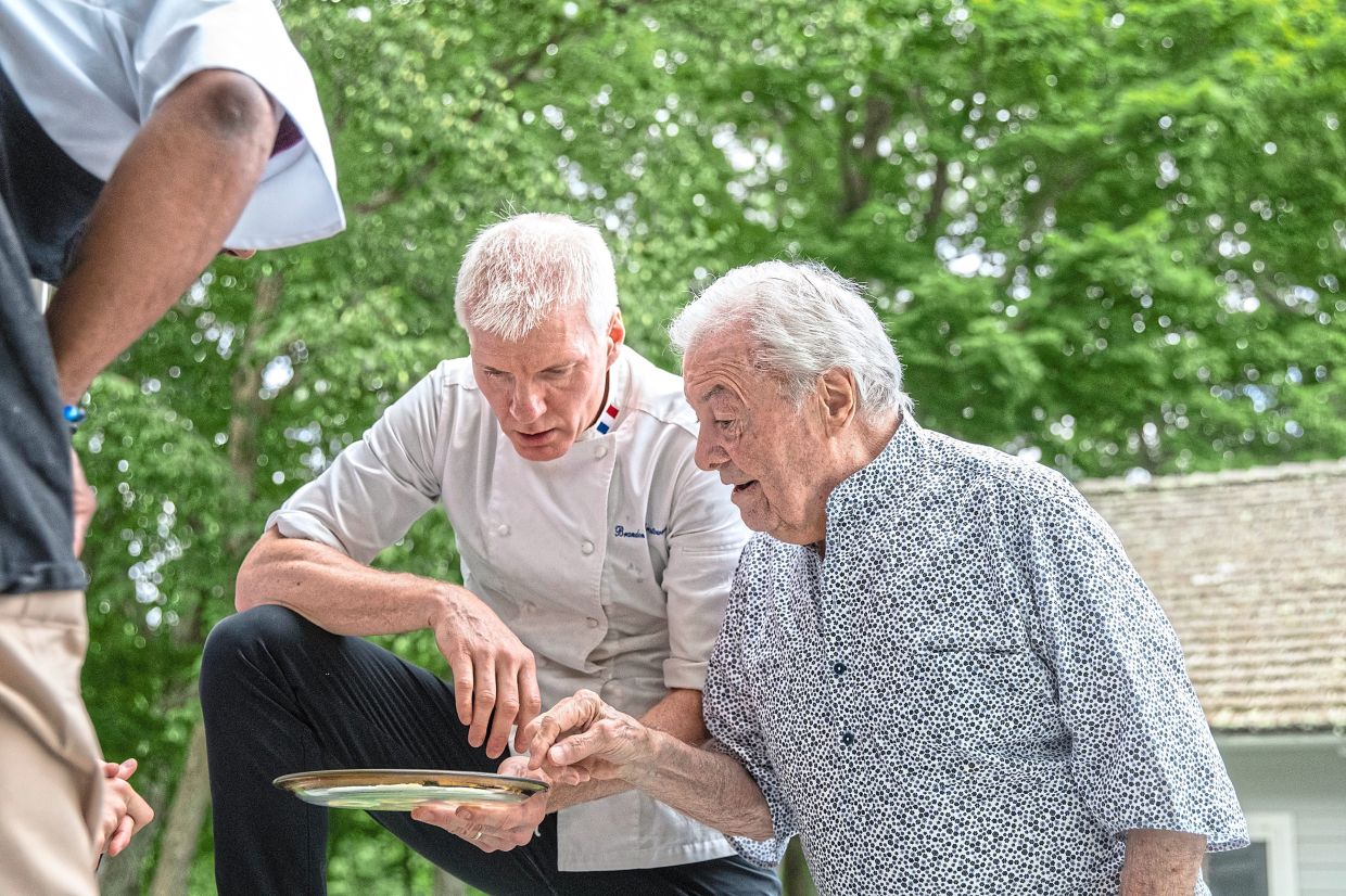 The chef Brandon Chrostowski, left, offers the chef Jacques Pépin a selection of oysters outside the kitchen during one of Pépin’s 90 birthday parties.