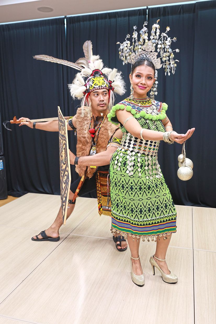 Syahidah and Amirul striking a pose in full Dayak traditional attire, complete with elaborate headgear and accessories used in Sarawakian dance performances.