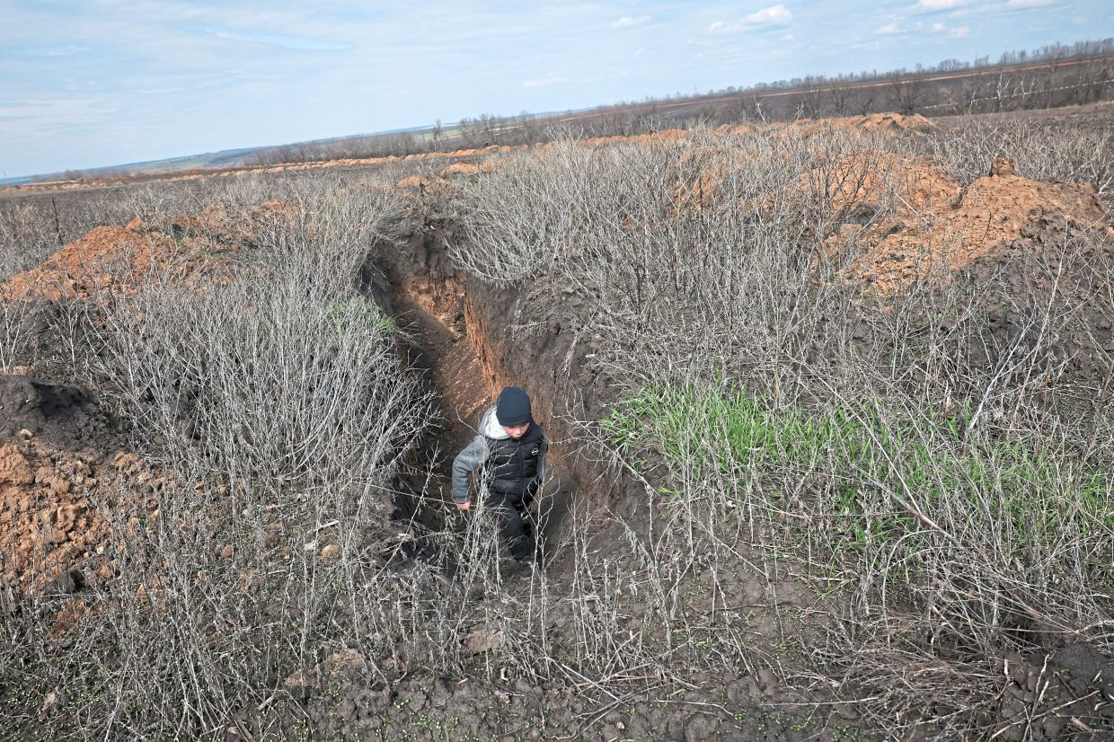 Maksym playing in a trench dug by Ukrainian forces in the outskirts of Kalynove. — Reuters