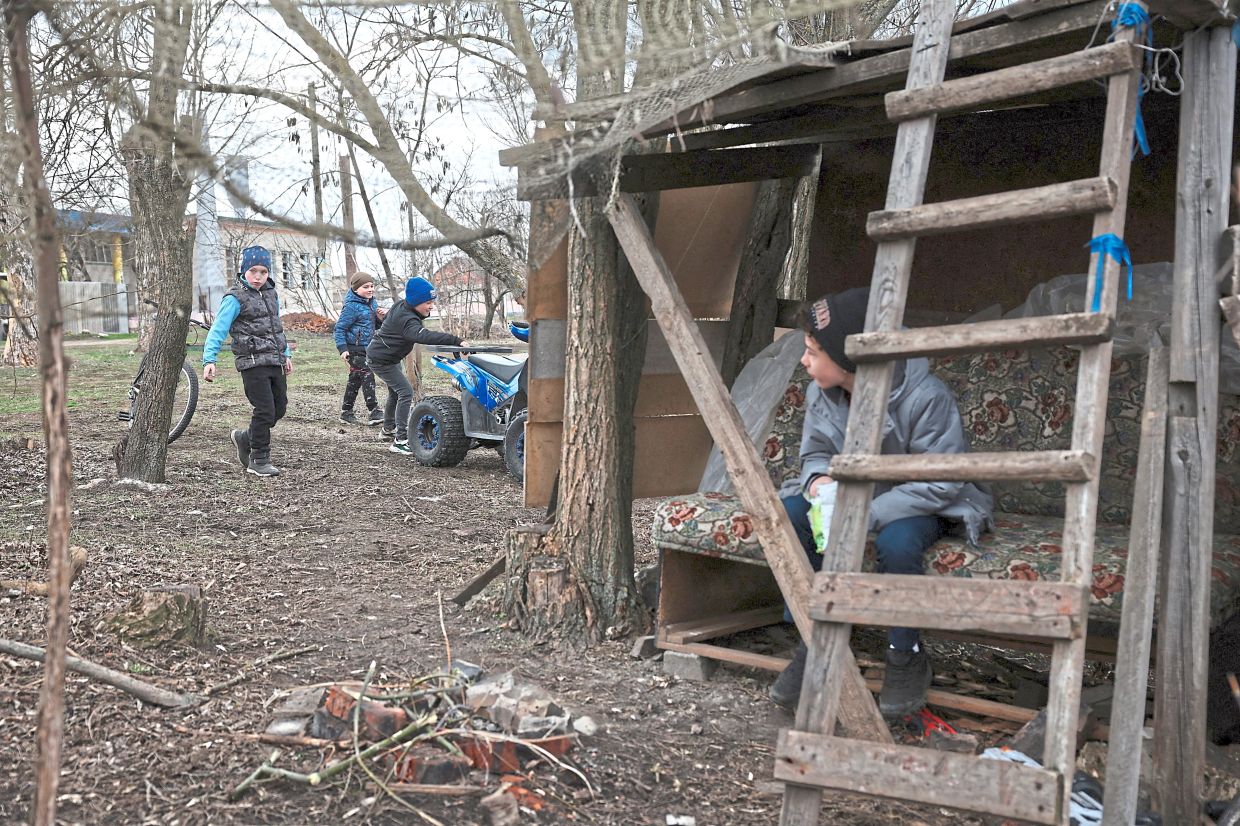 Vadim, 11, sitting in a make-believe army post as his friends Andrii, Maksym and nine-year-old Arseniy play with a quad bike in Kalynove, Kharkiv region. — Reuters
