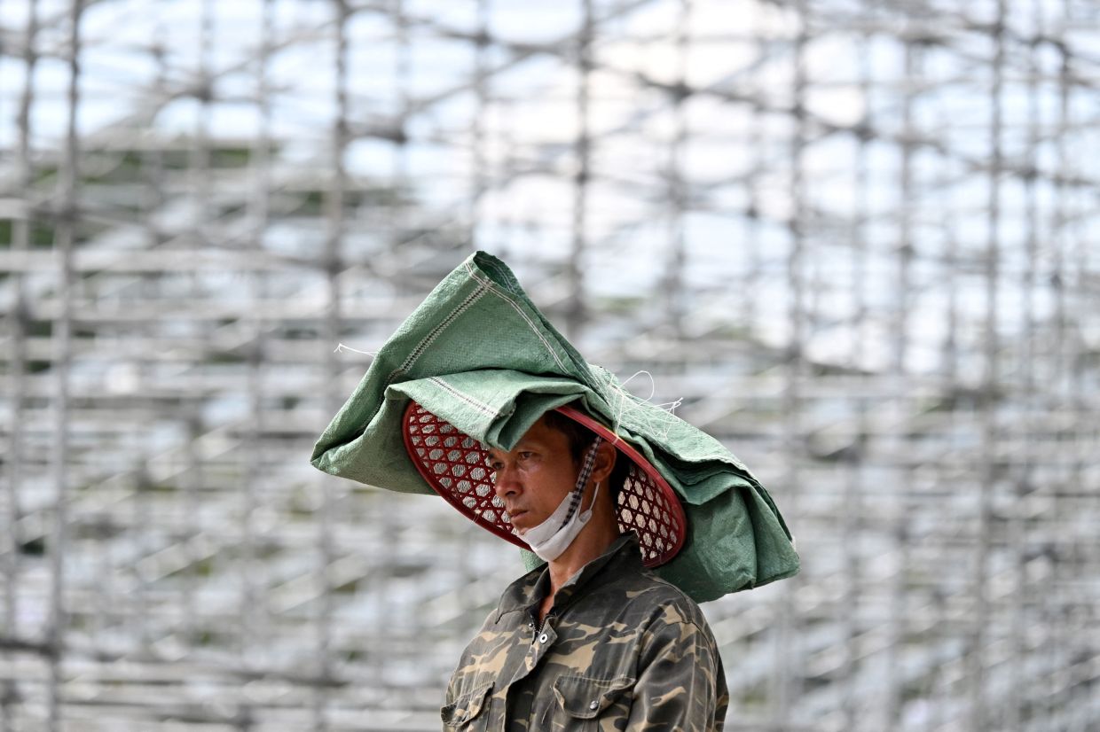 A worker uses a hat and a sack to protect himself from the sun in hot conditions while working at a construction site in Hanoi on Monday, August 4, 2025.-- Photo by Nhac NGUYEN / AFP