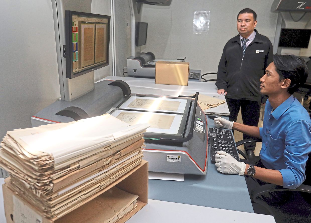 Zaidil Akmal (standing) observes as an archive assistant scans documents as part of the digitisation process.