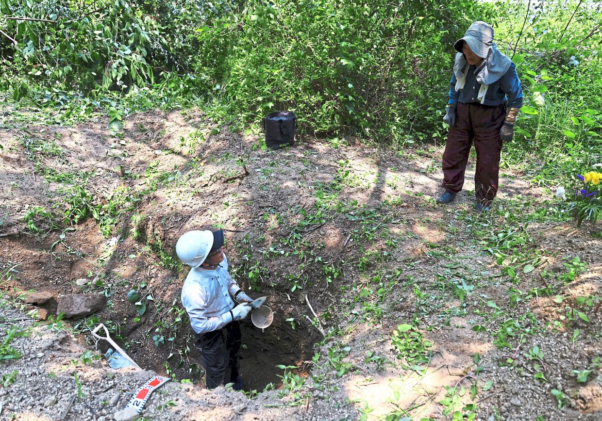 Tireless work: Kayo chatting with a local resident while digging a hole at a site on Ninoshima Island. — Reuters