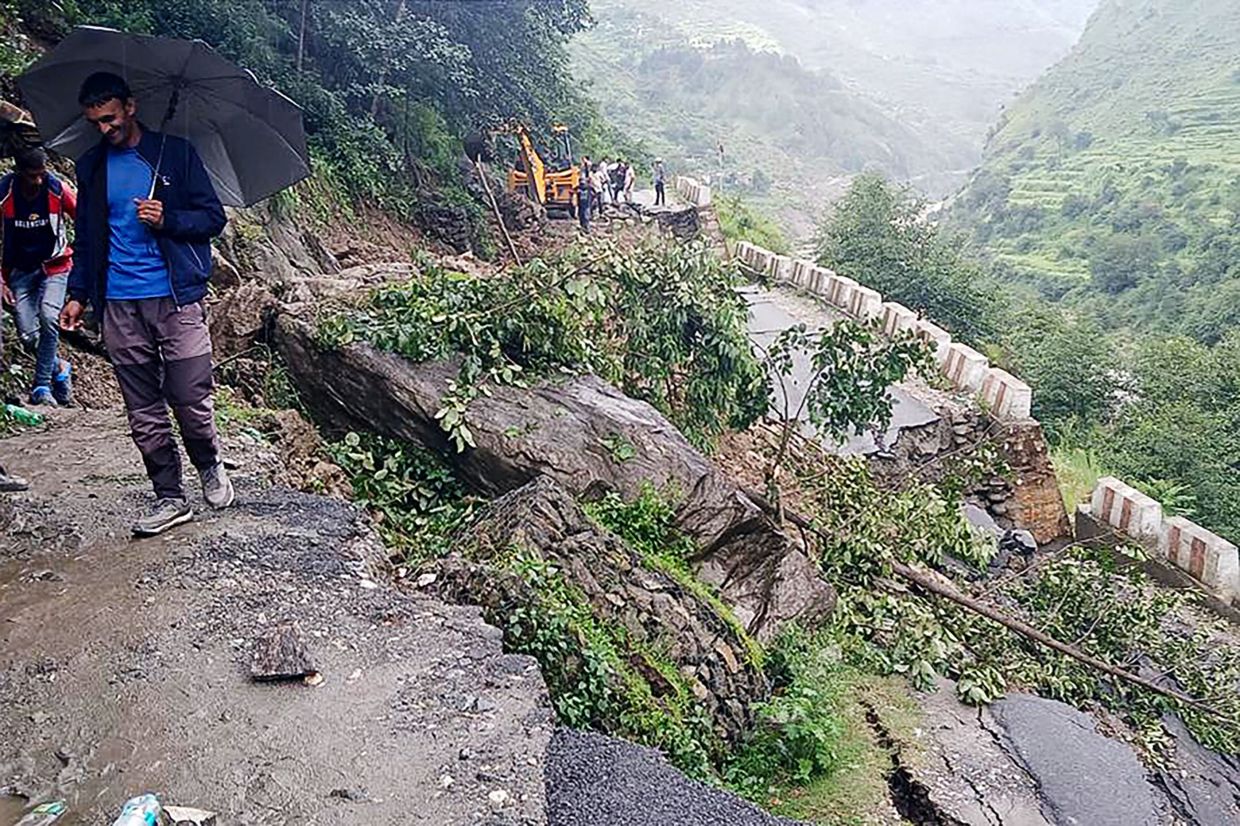 People stand beside a damaged road at a village near Uttarkashi on August 6, 2025, a day after a cloudburst caused a massive mudslide and flash floods in India's Uttarakhand state. The Indian army brought in sniffer dogs, drones and heavy earth-moving equipment to search for scores of people missing after the deadly Himalayan flash floods. At least four people were killed and more than 50 are unaccounted for after a wall of muddy water and debris tore down a narrow mountain valley, smashing into the town of Dharali in Uttarakhand state, rescue officials said on August 6. - Photo: AFP