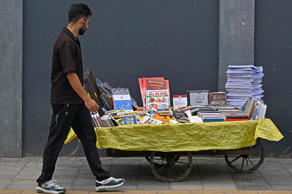 A pedestrian walks past a book cart along a roadside in Srinagar on Aug 7. Photo: AFP