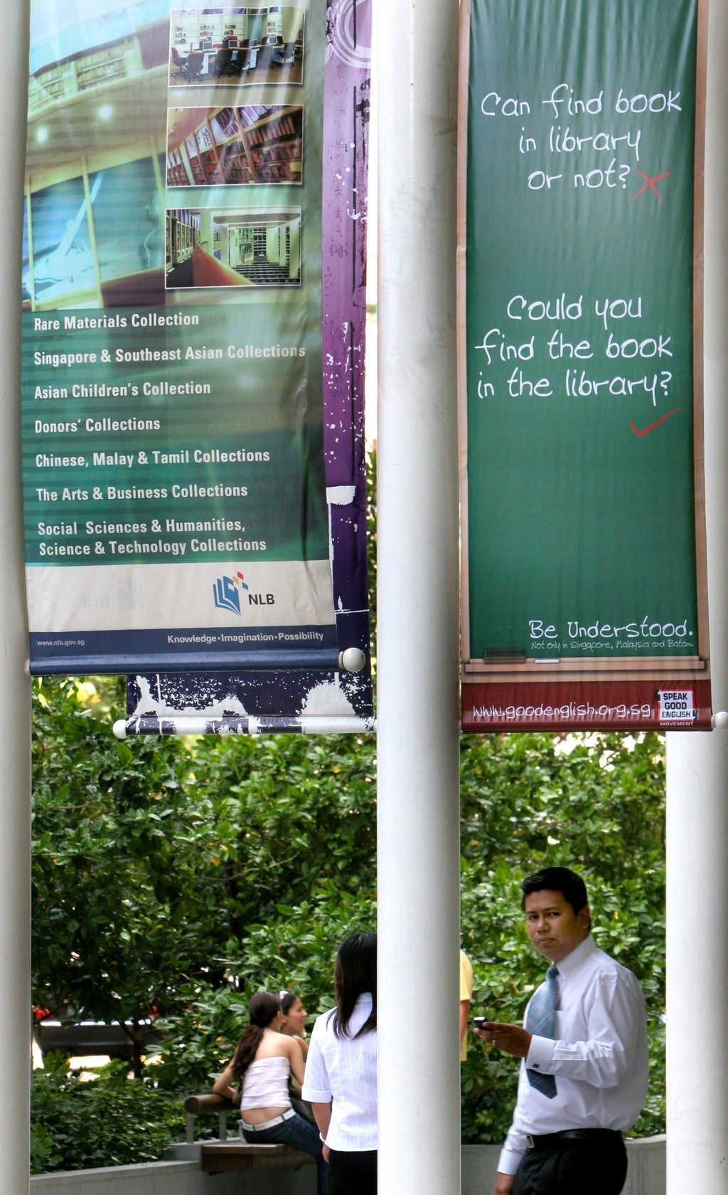 People walk under a banner that displays examples of correct spoken English and Singlish outside the Singapore National Library in 2006. -- Photo: AP
