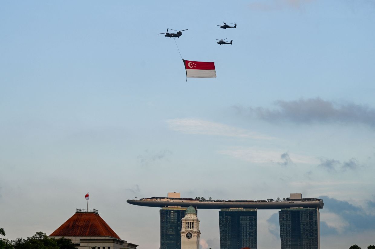 A Republic of Singapore Air Force C-47 Chinook (top L) and a pair of AH-64 Apache helicopters fly in formation with a giant Singaporean flag during celebrations marking the country's 60th National Day in Singapore on Saturday, August 9, 2025. -- Photo by Roslan RAHMAN / AFP