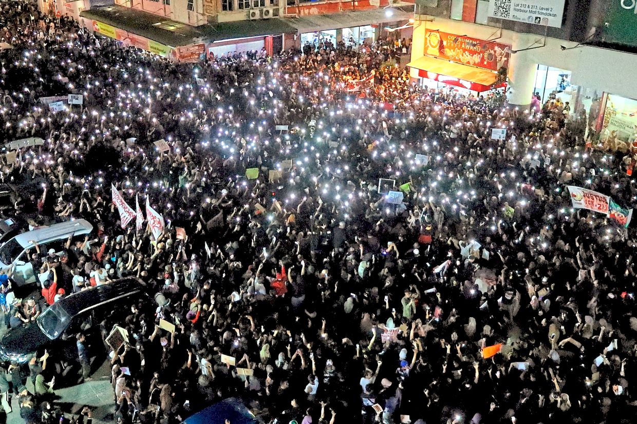 Beacon of hope: Participants at the Justice for Zara rally holding up their phones in Sandakan while (below) police officers guard the cemetery in Kg Masapol where the 13-year-old was laid to rest. — Bernama