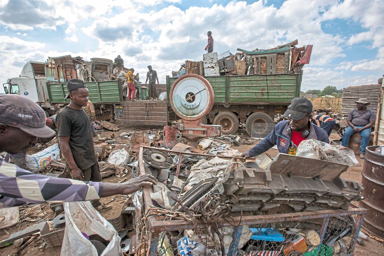 Workers load scrap metal onto a waiting truck to recycle at a collection site.