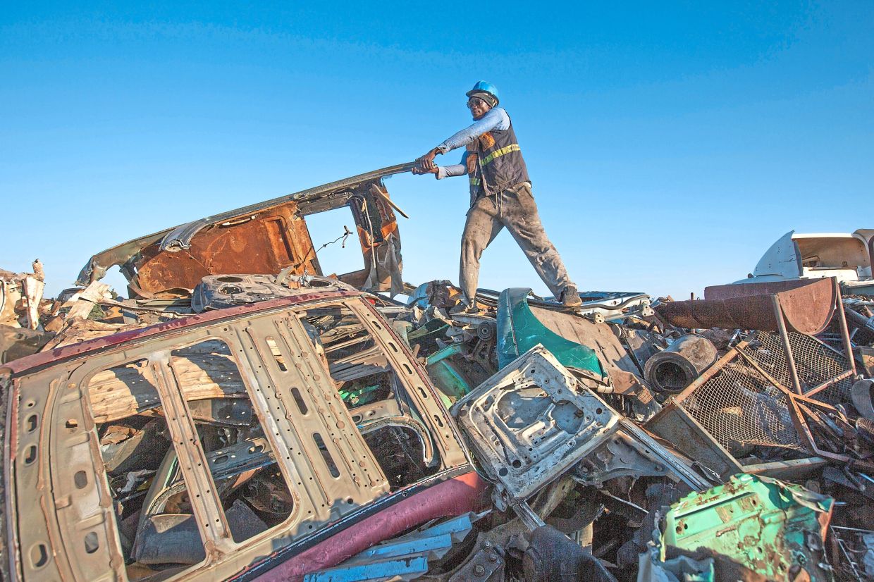 A man rearranges scrap metal at a collection site.