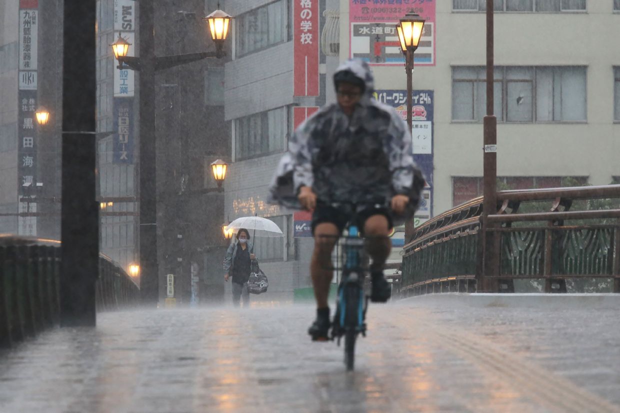People cycle and walk in heavy rain in the city of Kumamoto, Kumomoto prefecture, southwestern Japan, on August 11, 2025. Japanese authorities on August 11 urged millions to evacuate their homes after heavy rains unleashed floods and landslides in the country's southwest, leaving several residents missing. -- Photo by JIJI Press / AFP