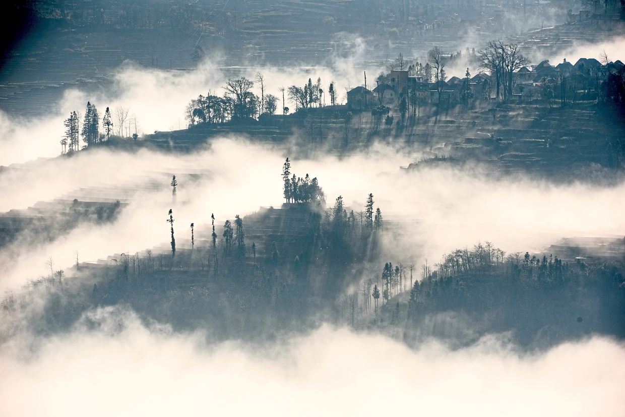 Morning mist draping over the terraced hills of Yuanyang, China, with distant villages emerging like islands in a sea of clouds.