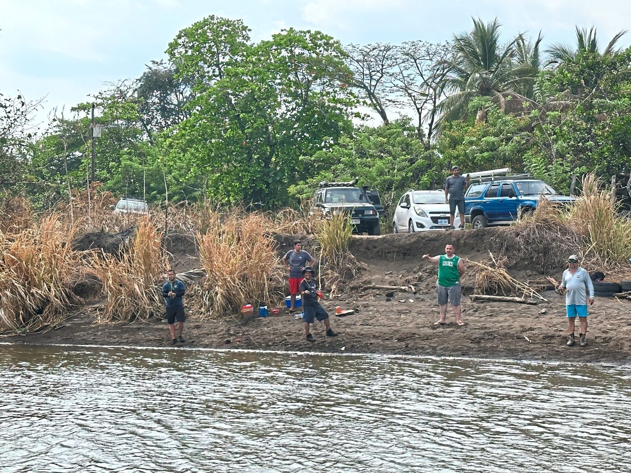 Anglers lining the sandy bank with their rods and trucks parked above, turning the river’s edge into a social fishing spot.