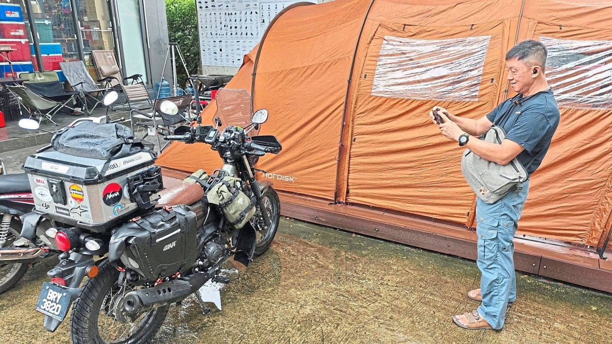 A rider taking a photo of the small Malaysian bike, a travelling companion that has carried its load faithfully across borders.
